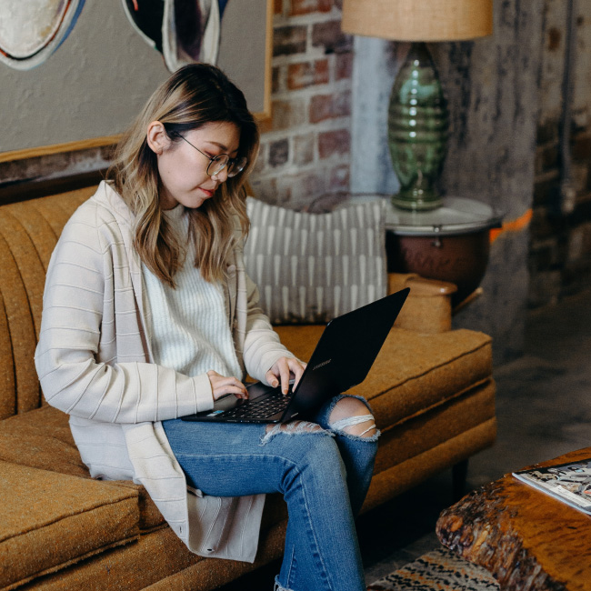 A woman engrossed in work on a couch, using a laptop to accomplish tasks efficiently and comfortably.