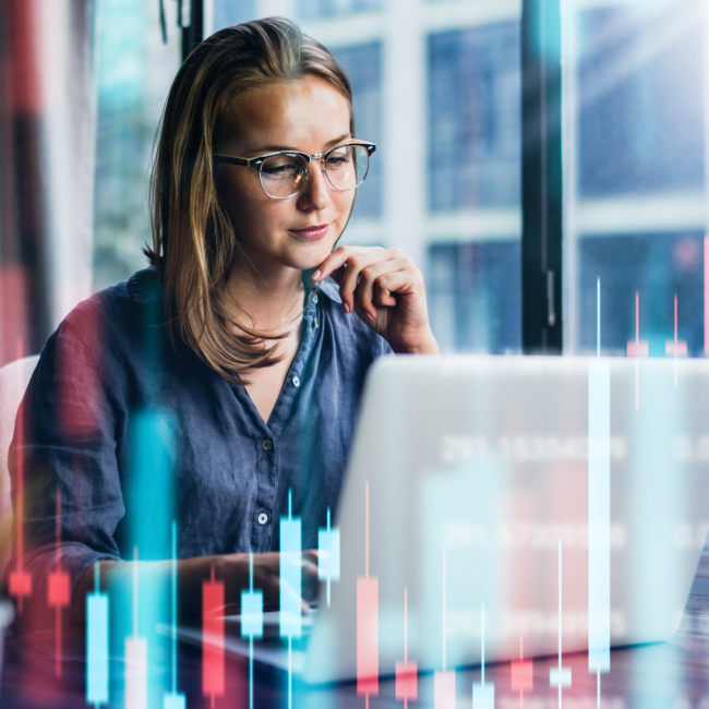 A woman wearing glasses studying financial data on a laptop.