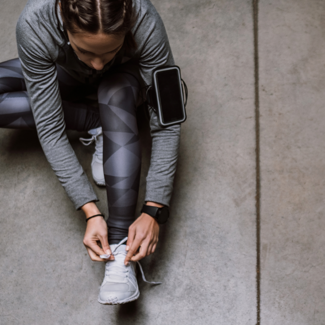 Una mujer se ata los zapatos en un suelo de cemento, preparándose para sus actividades diarias con concentración y determinación.