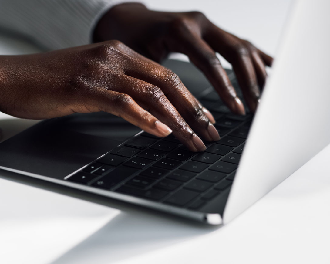 Close das mãos de uma mulher digitando em um laptop, concentrada e determinada.